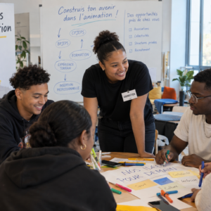 groupe de jeunes assis autour d'une table supervisé par l'animatrice de l'atelier